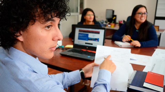 hombre joven señalando hoja de papel. él está en reunión con otras dos jóvenes.