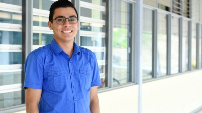 Estudiante de pie mirando al frente y sonriendo.