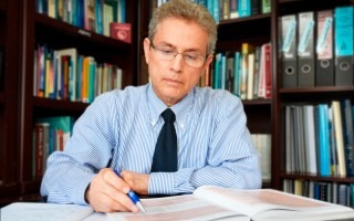 Hombre con corbata y lapicero en mano escribe en libro