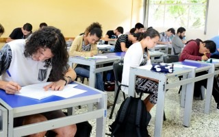 Imagen de varios estudiantes sentados en un pupitre en clases.