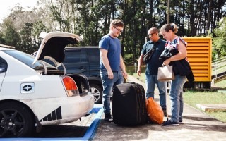 Imagen de un joven  con sus papás  bajando las maletas del carro para vivir en residencias.