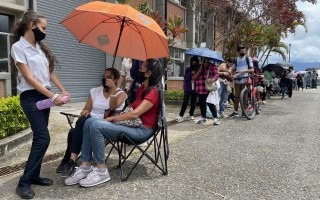 Personas haciendo fila con sombrillas para protegerse del sol.