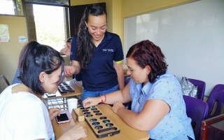 Imagen de una estudiante del TEC, una mamá y su hija aprendiendo matemática por medio de juegos.