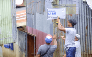 Tres hombres colocan un rótulo en un poste de madera.