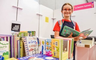 Nina posa junto, en uno de los stands mientras ve un libro 