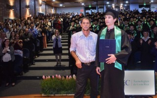 Joven graduado David junto  con su padre y detrás el auditorio con el resto de graduados