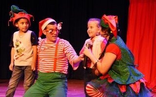 Dos personas sentadas hablando con una niña y un niño, en una obra de teatro.