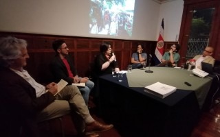 Los expositores y el moderador del conversatorio escuchan la exposición de Zuhra Sasa.