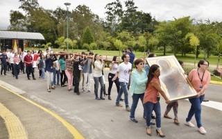 Imagen de funcionarios y estudiantes cargando una cruz y un cuadro con la imagen de la Virgen.