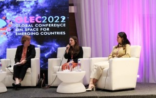 Se observan tres mujeres en el escenario, en un panel de discusión.