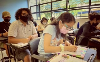 jóvenes en una clase en el TEC. La principal es una muchacha tomando notas. 