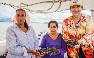 tres mújeres enseñan mejillones recien sacados del mar.