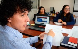 hombre joven señalando hoja de papel. él está en reunión con otras dos jóvenes.