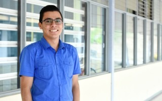 Estudiante de pie mirando al frente y sonriendo.