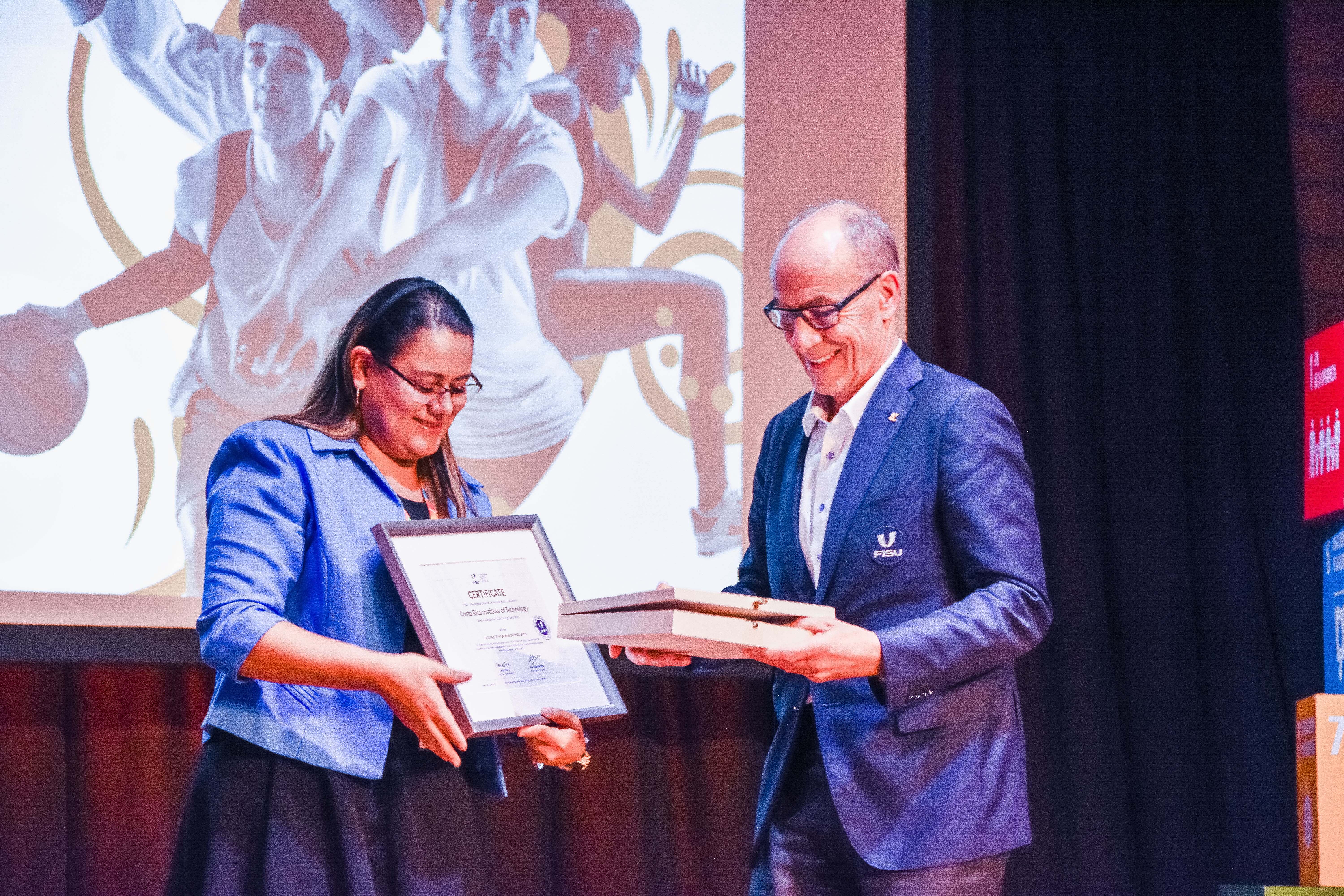 La vicerrectora María Teresa Hernández Jiménez recibe los certificados de Campus Saludable de parte del presidente FISU, Leonz Eder. Fotografía de Pablo Quesada. La vicerrectora recibe dos certificados.