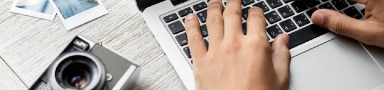 Imagen de unas manos en una computadora y una cámara