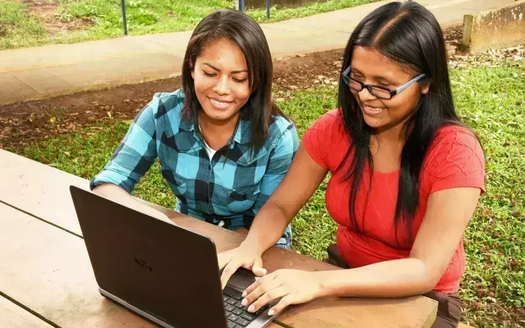 Estudiantes indígenas sentadas utilizando computadora.